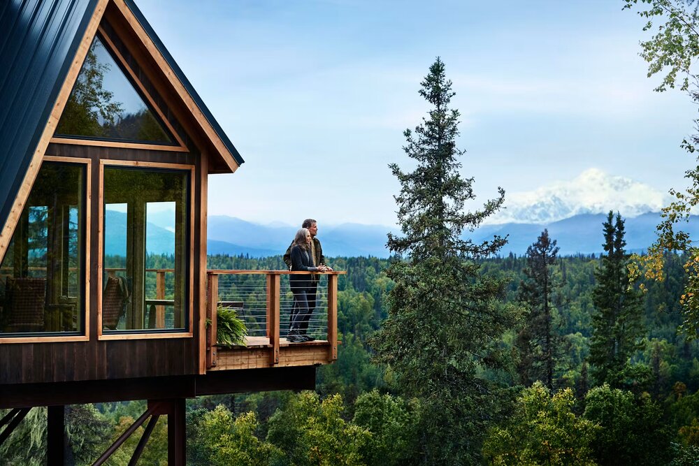 Guests on the deck of a custom-built treehouse with Denali in view